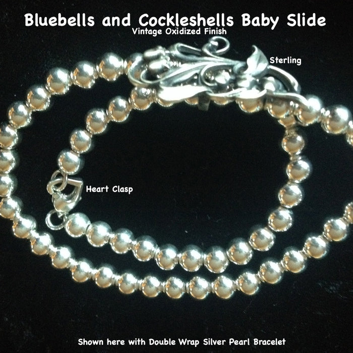 This  pretty and delicate little slide has such detail and femininity. Slip an ecru wired ribbon through this slide and tie it as a choker for a simple, romantic look. Comes with a beautiful ribbon.  Sterling Silver Bluebells and Cockleshells Baby Slide. Part of a beautiful trio of slides which also are beautiful on my Double Wrap Silver Pearls Bracelet.  1-3/8" x 5/8 approximately. Hand made in the USA. Hand Signed.  SILVER PEARLS DOUBLE WRAP BRACELET SOLD SEPARATELY.