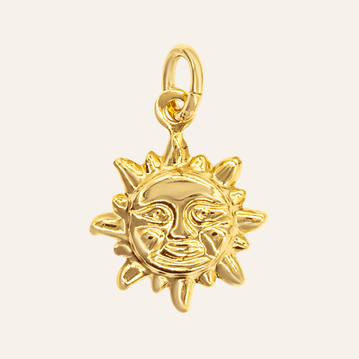 A polished gold sun charm with a smiling face and radiating rays, attached to a gold loop at the top, shown on a light cream background.
